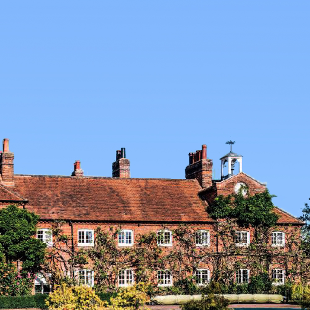 The Clock House, a long, red brick building with many windows, covered in climbing plants and with a large clock at one end